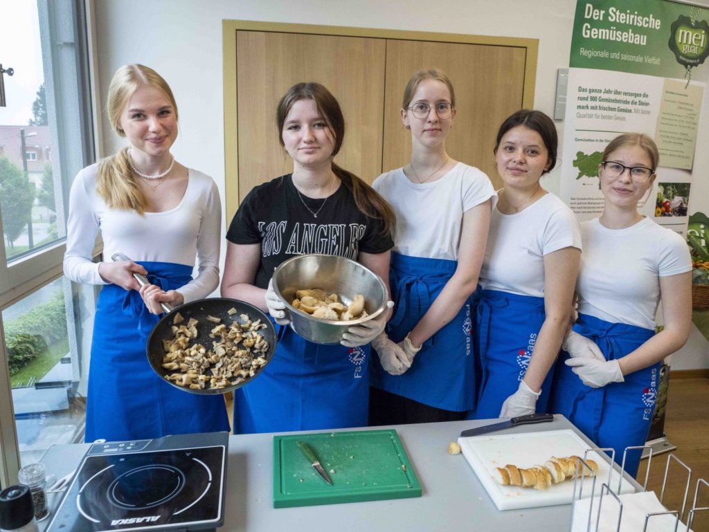 Fünf Mädchen mit blauen Schürzen zeigen sich beim Kochen von Pilzen beim Veggie-Day