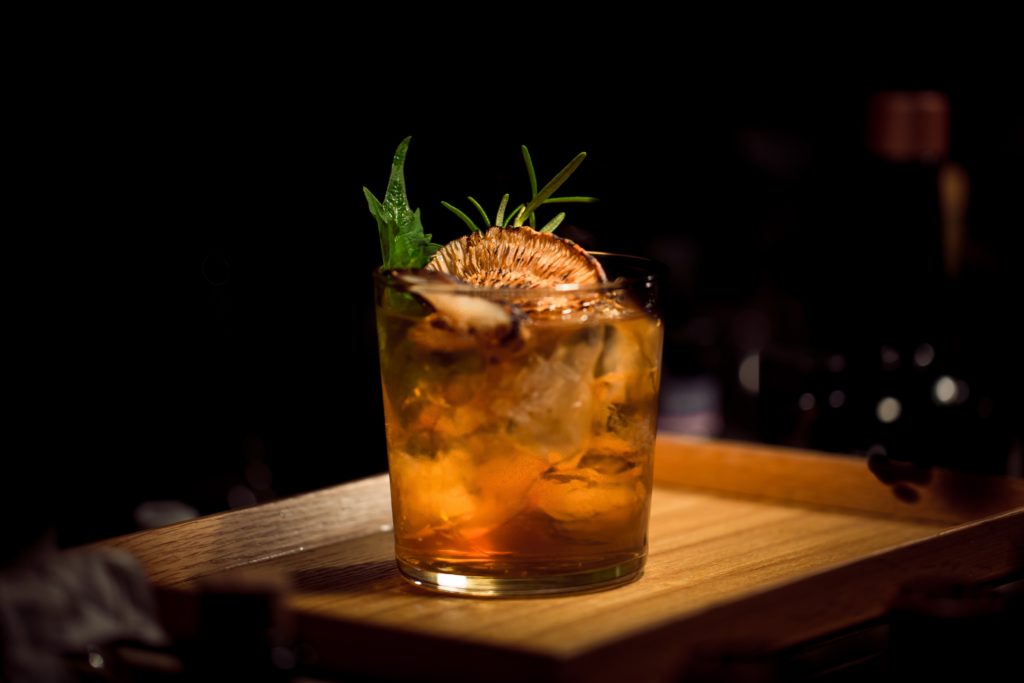 In einer Bar. Vor dunklem Hintergrund ein niedriger oranger garnierter Cocktail