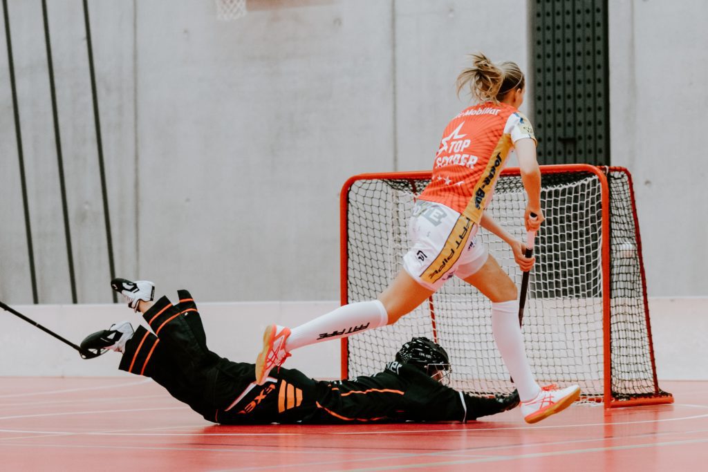 Eine Floorballspielerin schießt ein Tor während die Torwärtin sich auf den Boden wirft. 