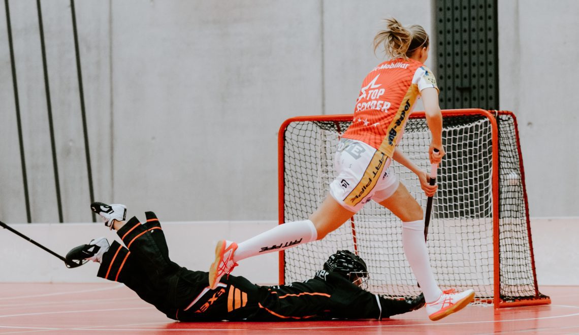 Eine Floorballspielerin schießt ein Tor während die Torwärtin sich auf den Boden wirft.
