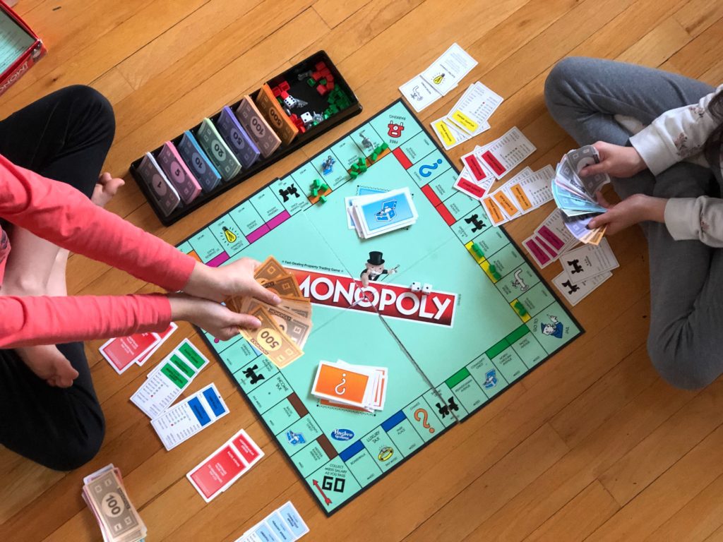 Zwei Kinder sitzen am Boden um ein Monopoly-Board.