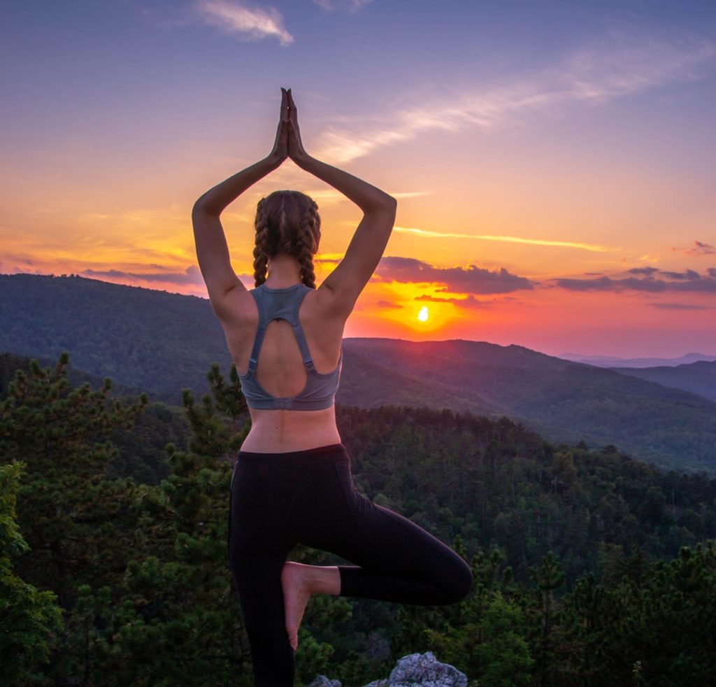 Eine Frau macht eine Yoga-Pose am Berg zum Sonnenuntergang