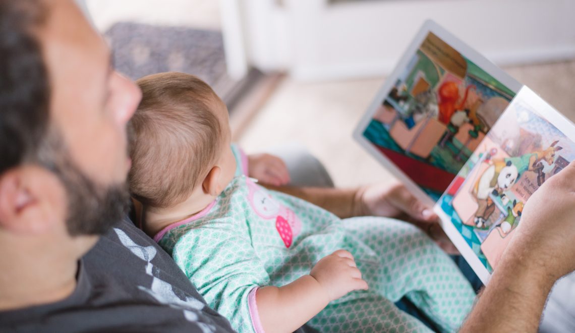 Ein Vater liest dem auf seiner Brust liegenden Kind aus einem Bilderbuch vor